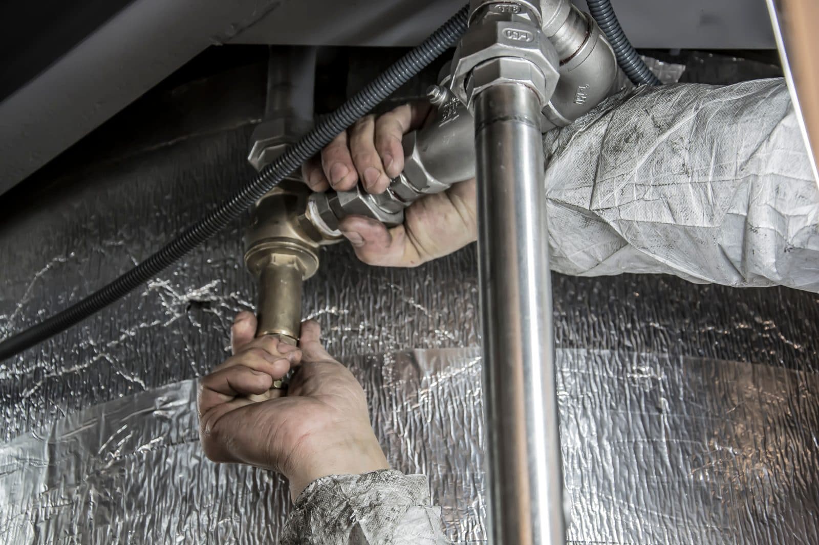 Plumber's hands fitting and tightening a pipe connection beneath a sink