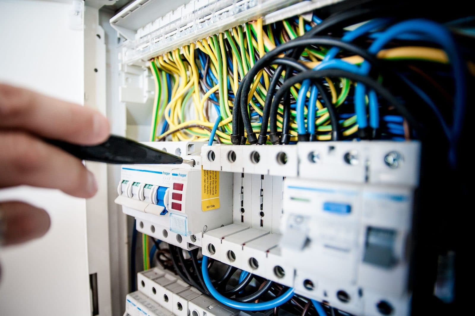 Electrician's hand working inside an open distribution board, adjusting a circuit breaker among colour-coded wiring