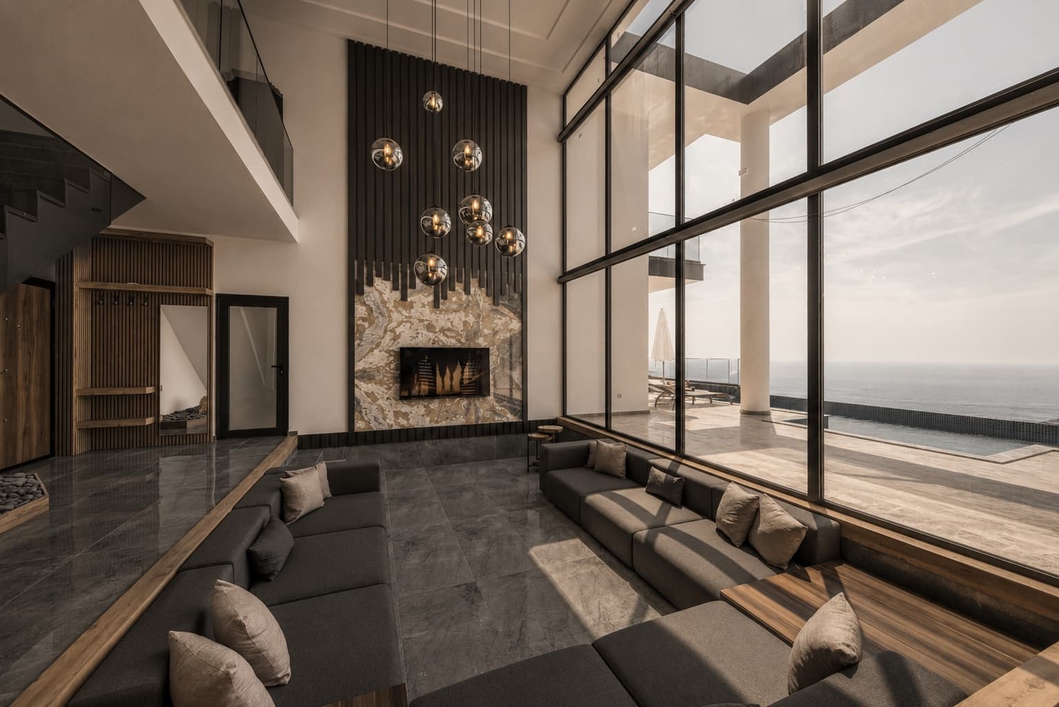 Spacious modern living room with high ceilings, pendant lighting and a sea view through floor-to-ceiling glass