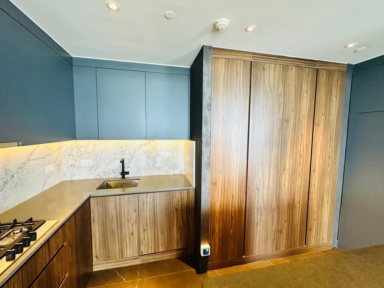 Kitchen carpentry featuring a tall wood-finish pantry unit, blue upper cabinets and a marble-look backsplash.