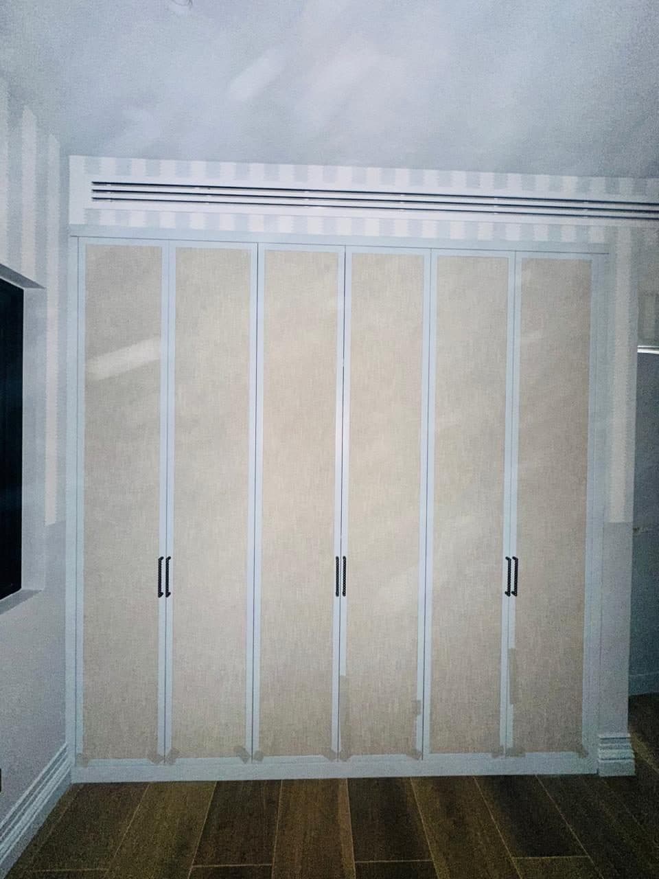 Built-in floor-to-ceiling wardrobe with fabric-panel doors and bar handles, fitted beneath a linear AC supply grille.