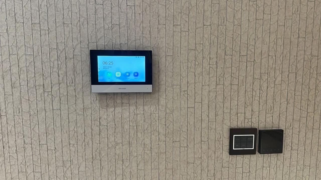 Wall-mounted video intercom panel installed alongside smart wall switches and controllers as part of a home automation fit-out.