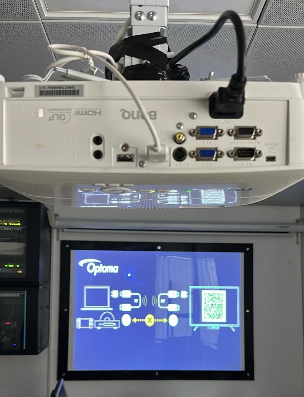 Ceiling-mounted projector with routed cabling above a wall-mounted setup screen, installed with the server rack below.