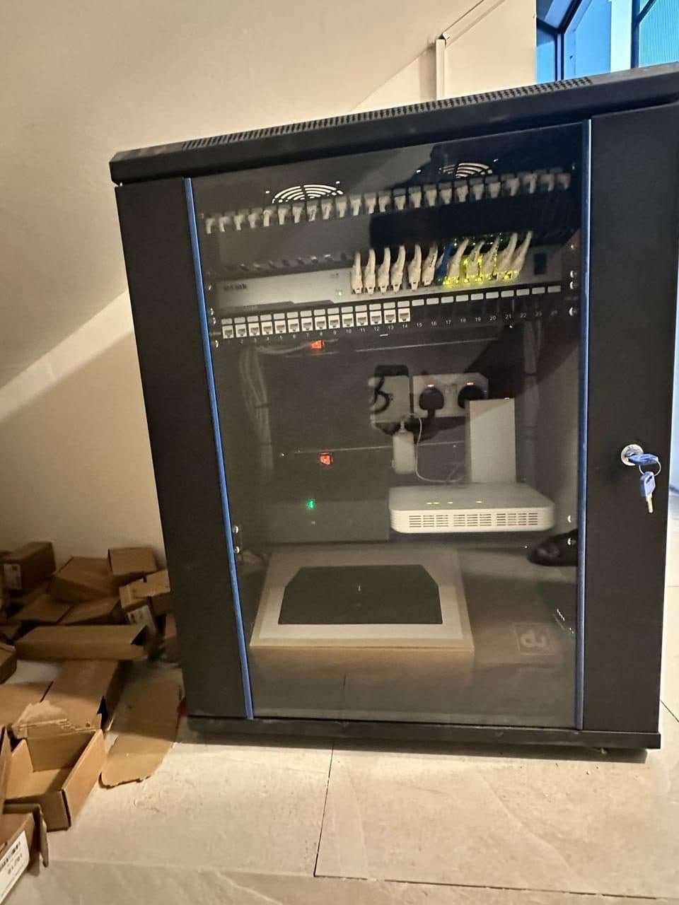 Wall-mounted network cabinet with switch and patch panel, closed up and commissioned at the end of a structured cabling job.