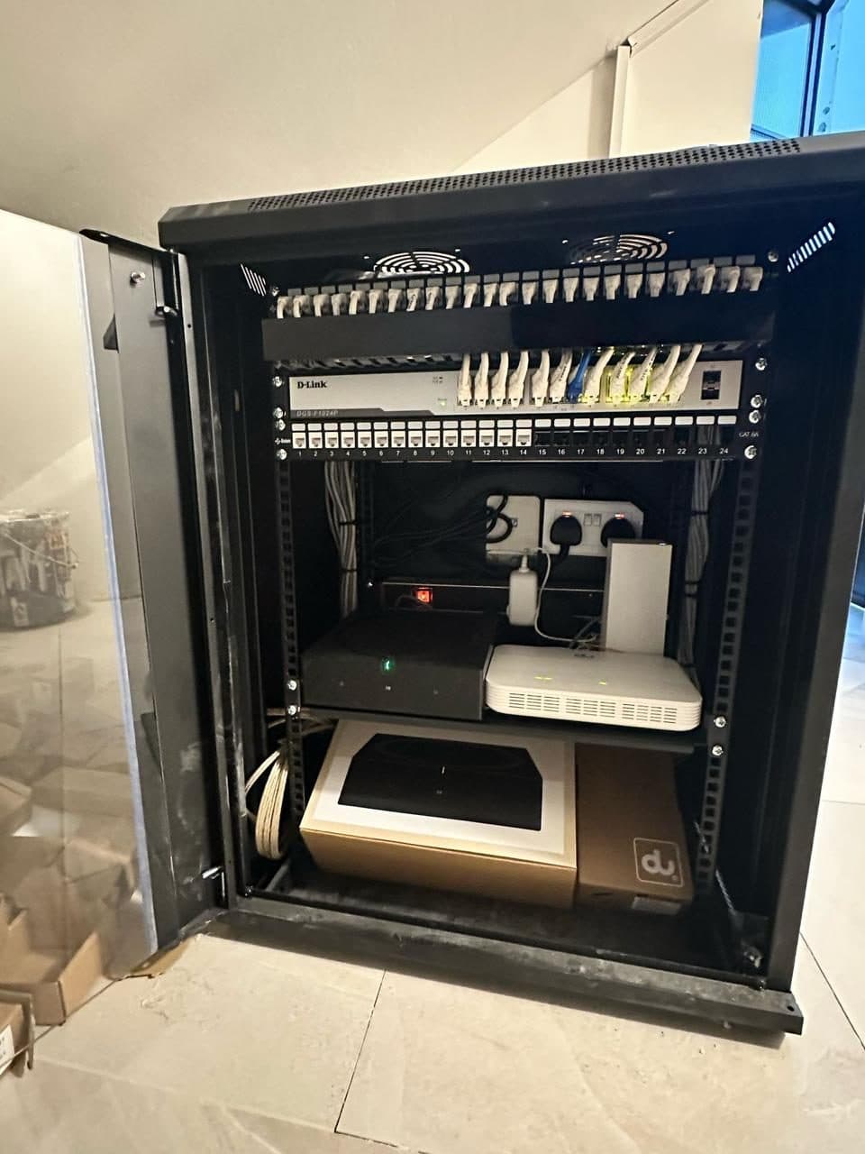 Open network rack cabinet showing the switch, patch panel and router mid-installation, cables still being routed and dressed.