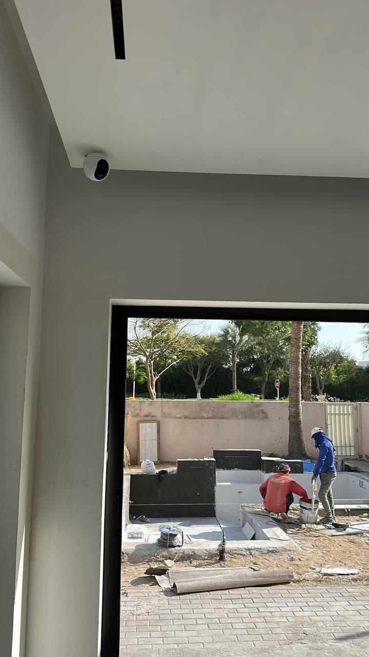 Dome CCTV camera mounted on an interior ceiling corner, positioned to monitor an active construction area through the open door.