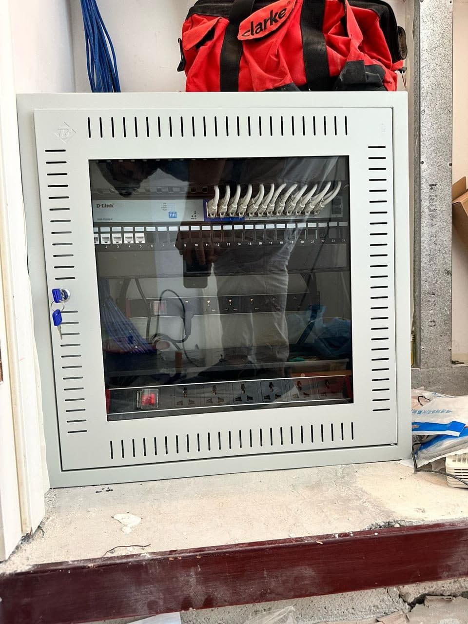 The same wall-mounted network cabinet secured behind its glass door, cabling visible and ready for client handover.