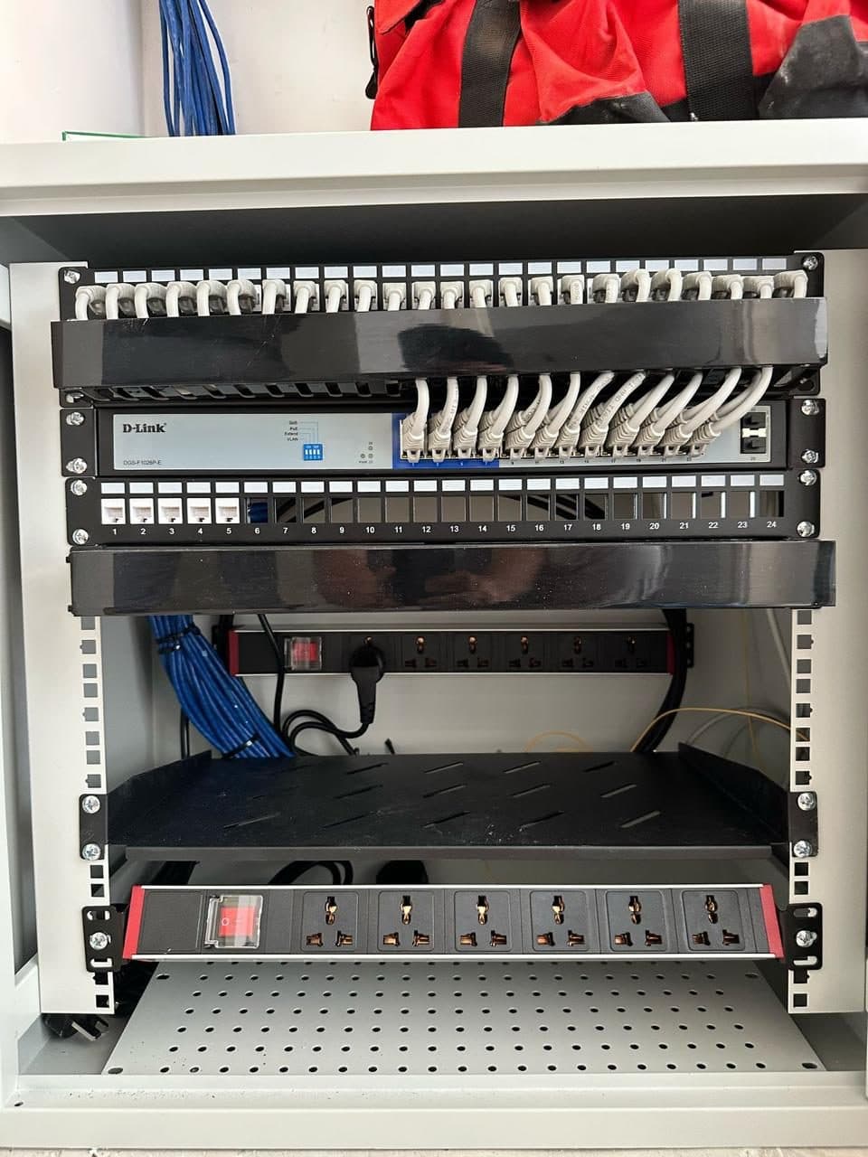 Open network rack showing a switch and patch panel with cables freshly terminated during an on-site cabling job.