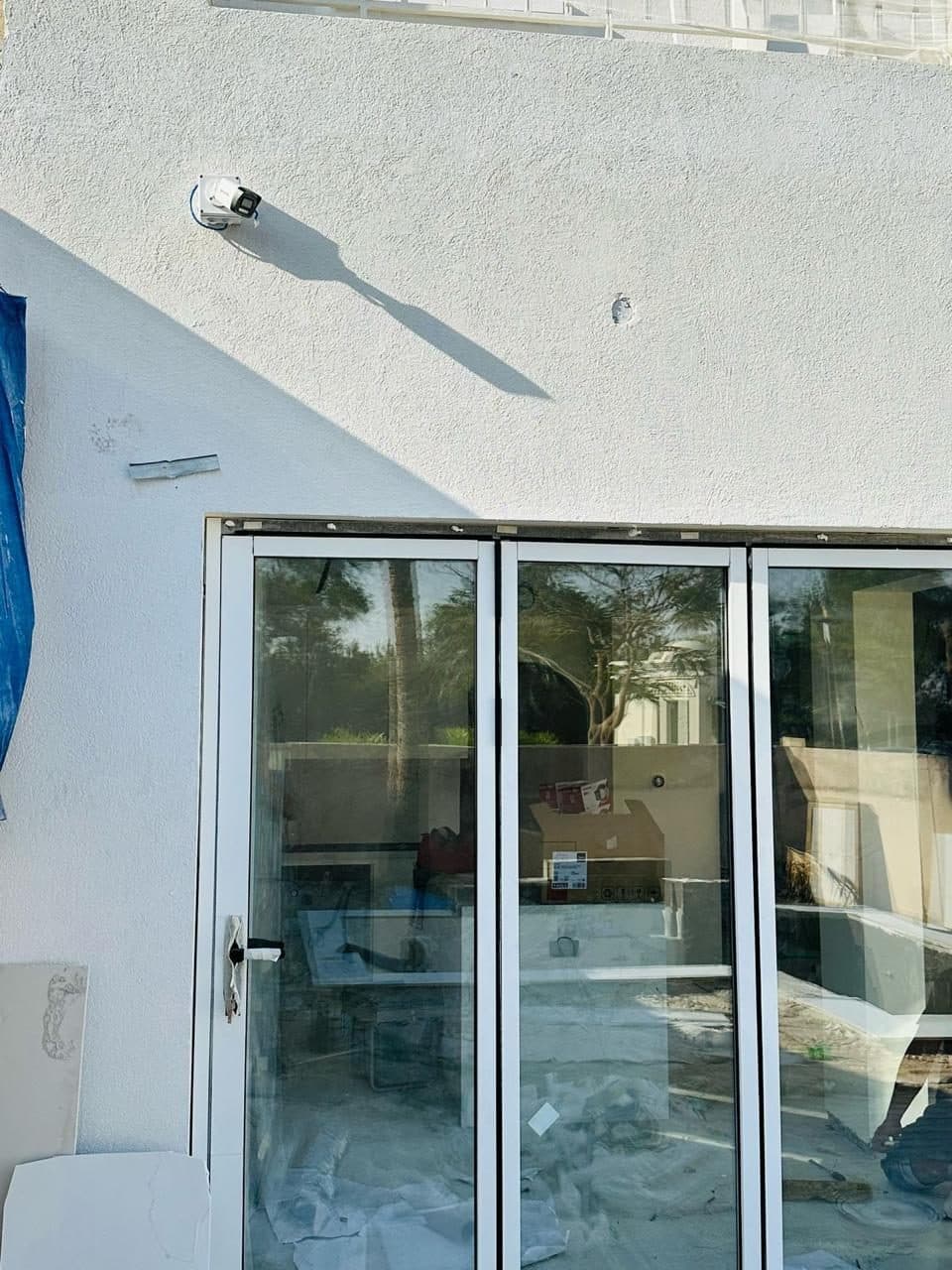 Dome CCTV camera mounted on an exterior wall above aluminium bifold glass doors, covering the garden approach.