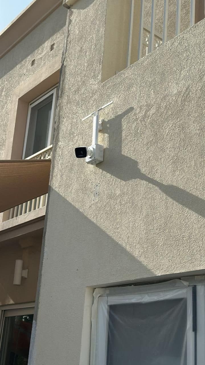 Bullet-style CCTV camera mounted on a villa's exterior stucco facade near the balcony line for perimeter coverage.