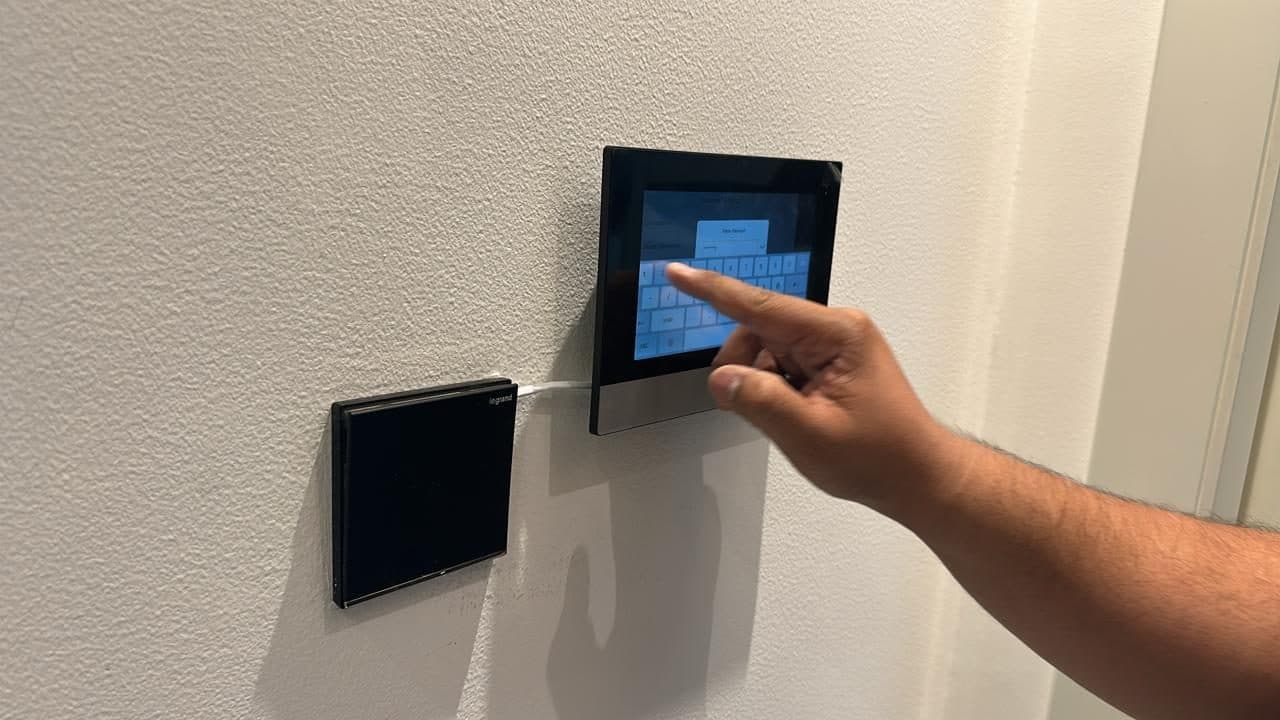 A technician programming a wall-mounted touchscreen home automation and intercom panel during commissioning.