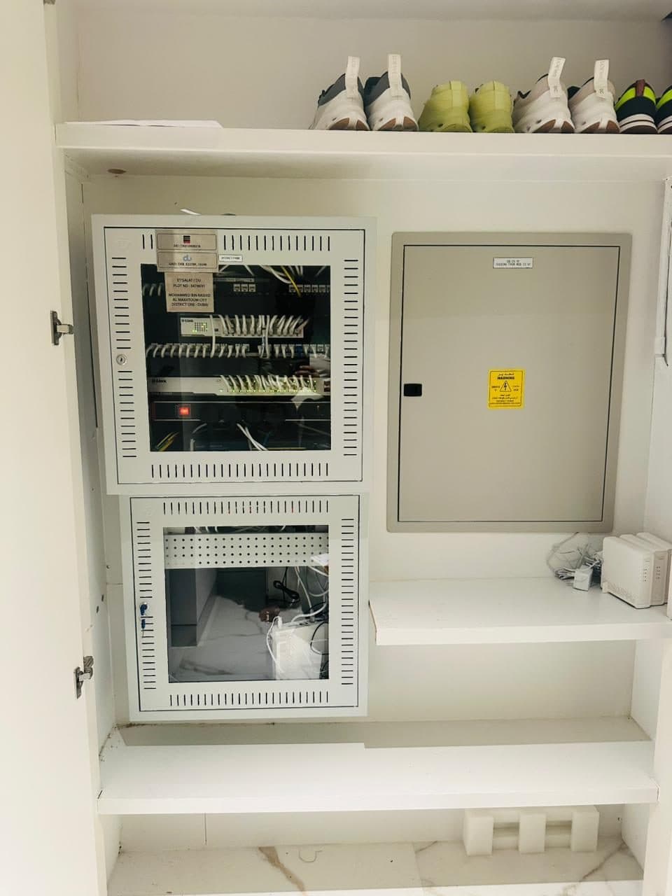Close-up of an open network rack with patch panel and switch installed alongside the property's electrical distribution panel.