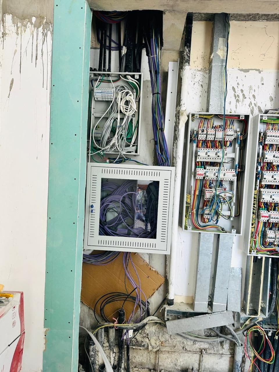 Several electrical distribution boards and cabling cabinets installed during an active construction fit-out, conduits still exposed.