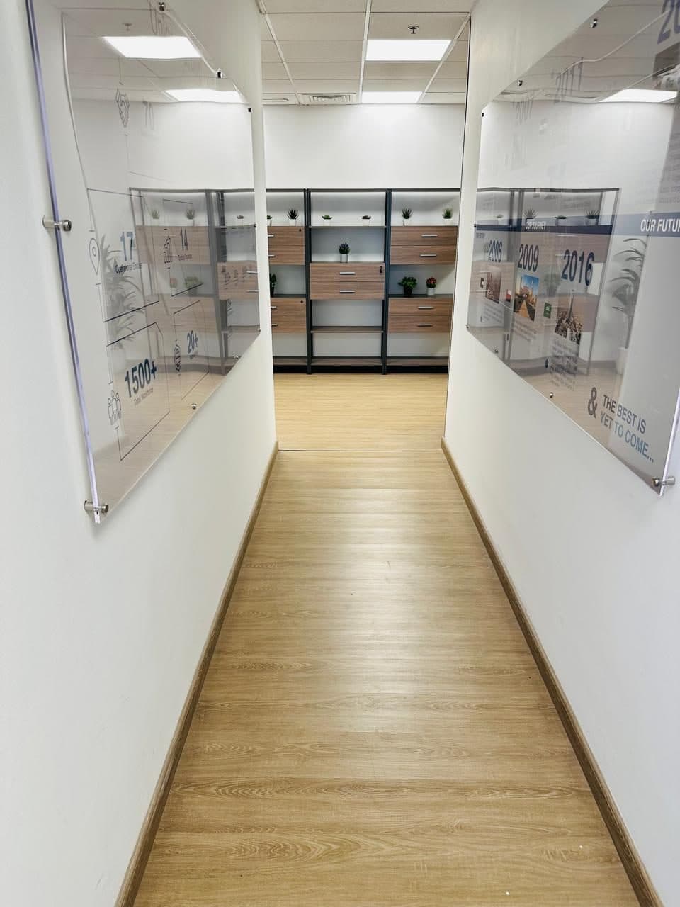 Finished office corridor leading to a display area with built-in wood-toned shelving and framed wall panels.
