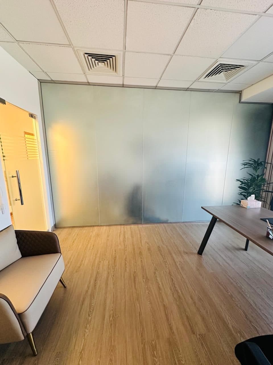 Floor-to-ceiling frosted glass partition dividing an office space, finished alongside wood flooring and a built-in desk.
