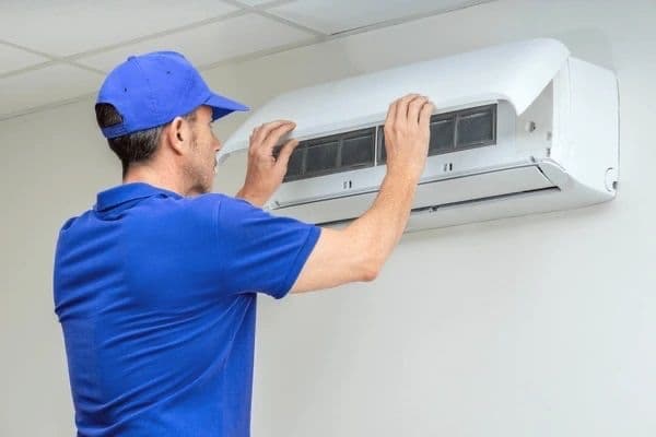 Technician in a blue uniform installing an indoor split AC unit on a wall