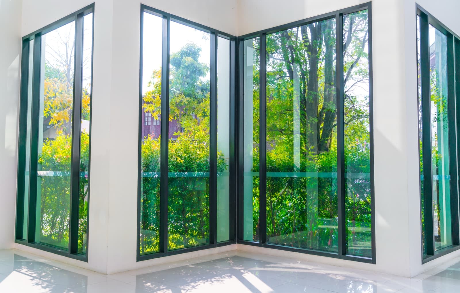 Floor-to-ceiling black aluminum window frames in a bright corner room overlooking greenery