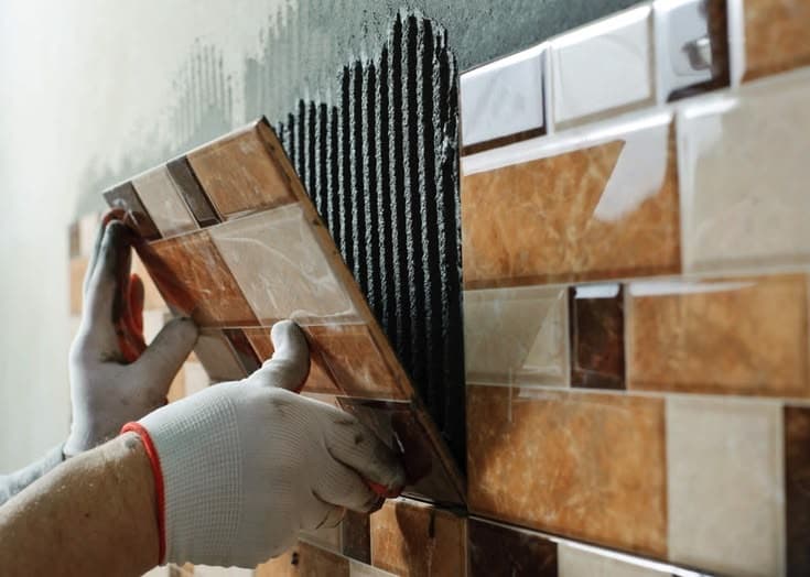 Tiler applying adhesive with a notched trowel before fitting a bathroom wall tile