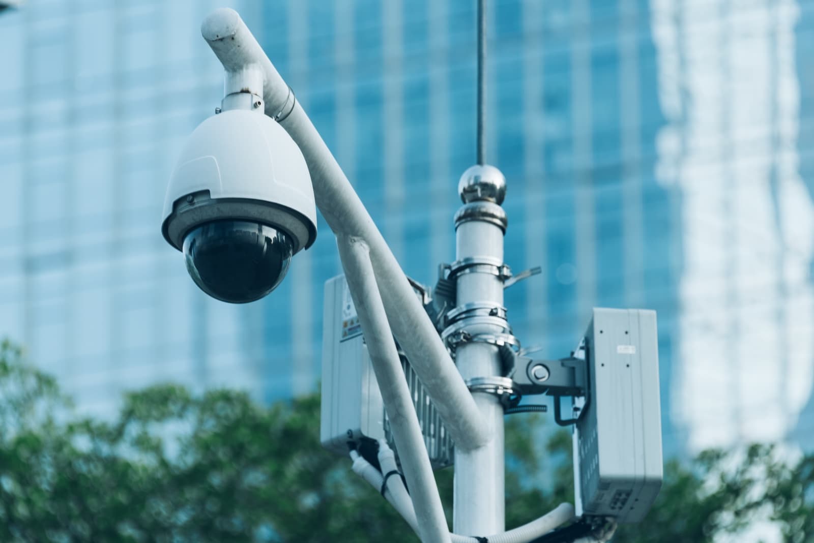 Dome CCTV security camera mounted on an exterior pole against a city backdrop