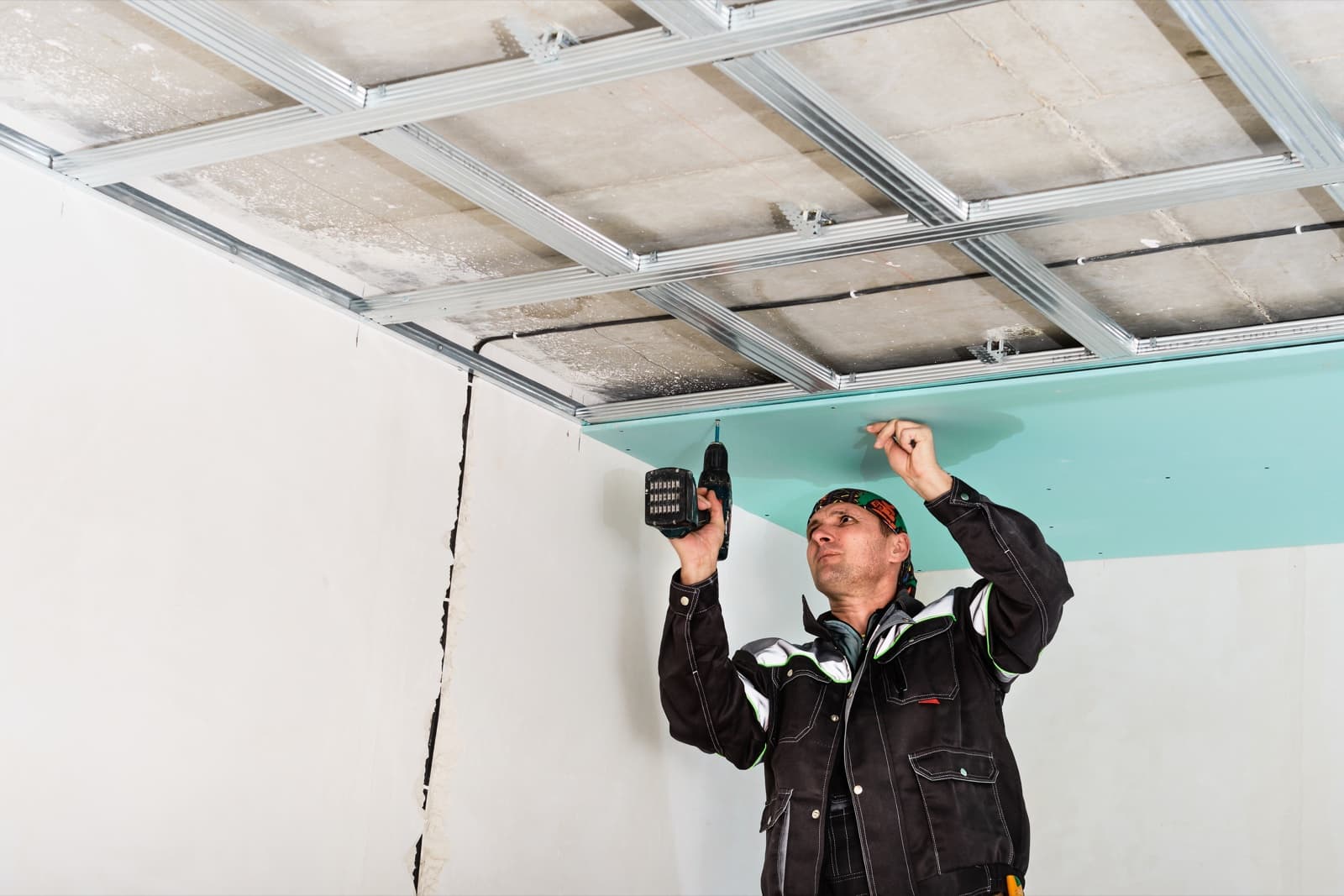 Worker drilling a board into a metal false ceiling frame during installation