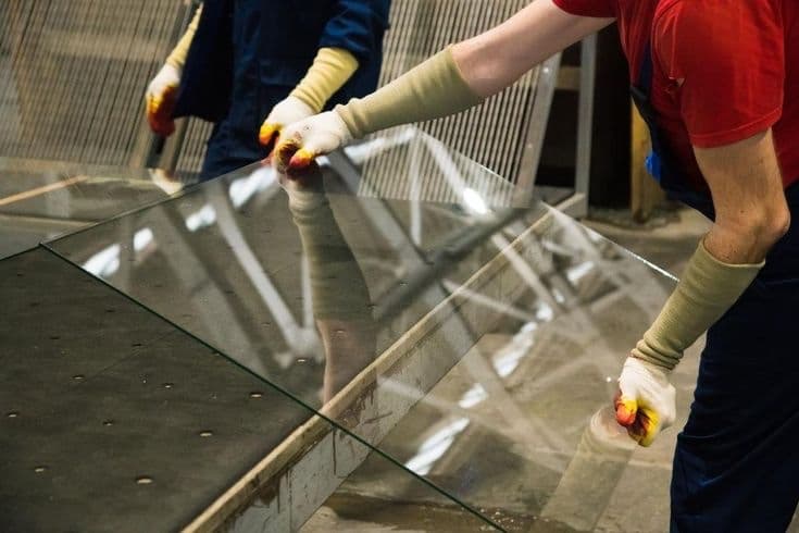 Workers in protective gloves handling a large glass panel in a workshop