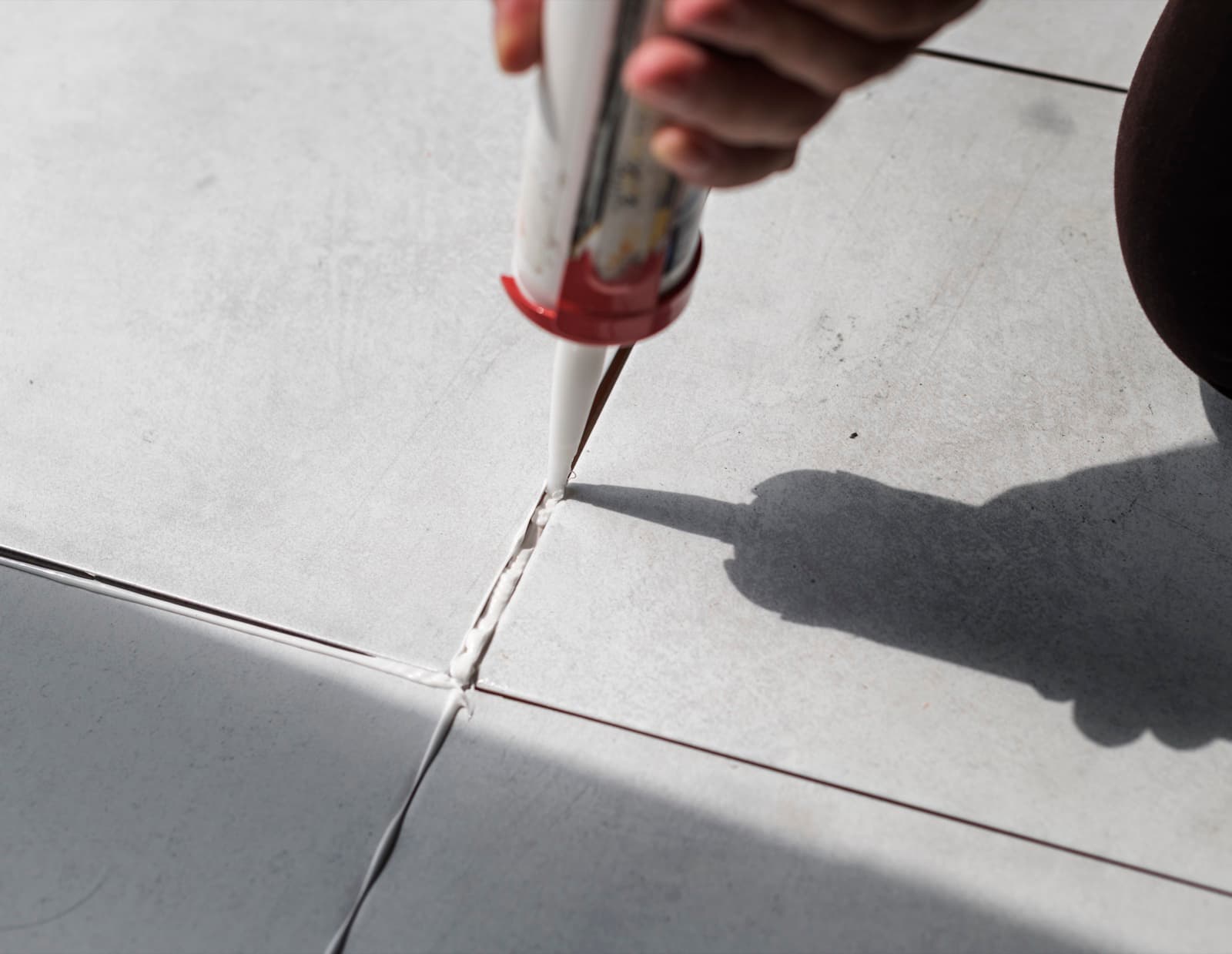 Sealant being applied along a tile joint with a caulking gun