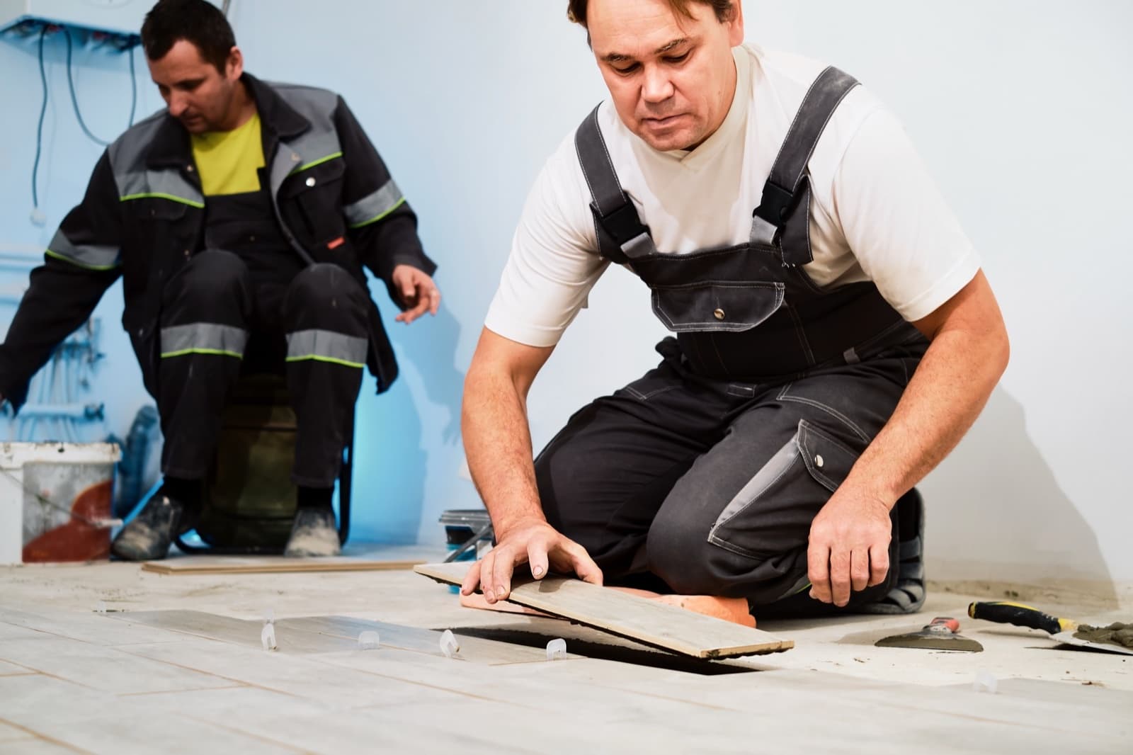 Workers fitting a replacement floor tile using plastic leveling spacers