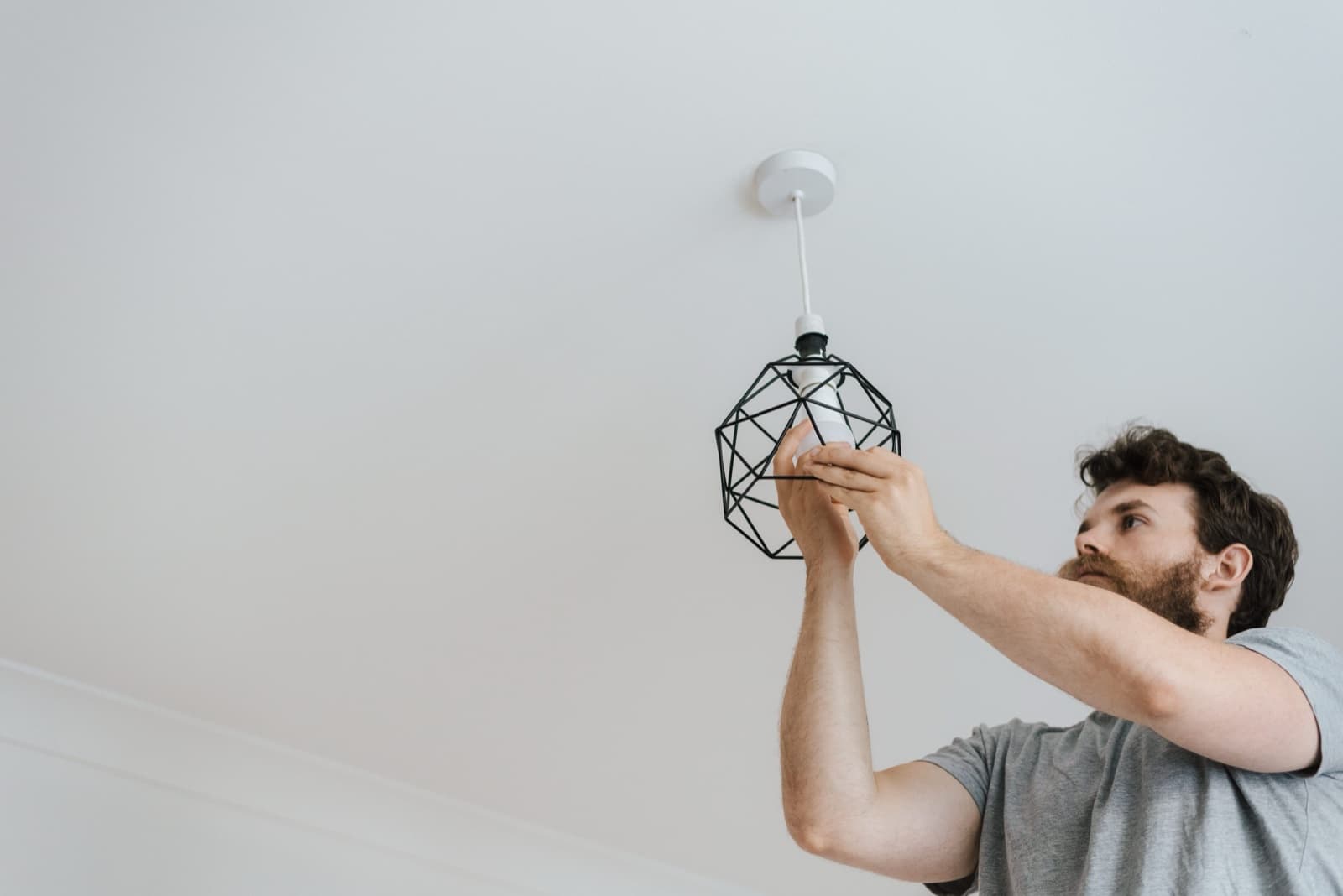 Electrician fitting a wire-cage pendant light fixture to a ceiling rose